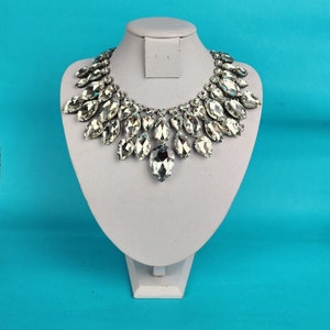 May include: A silver necklace with a large, teardrop-shaped crystal pendant and smaller crystals surrounding it.