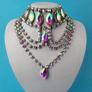 May include: A multi-layered iridescent crystal necklace with a teardrop pendant. The necklace is made of small, faceted crystals that are strung together on a silver chain. The pendant is a large, teardrop-shaped crystal that is also iridescent.