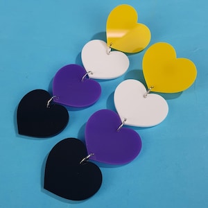 May include: A pair of dangle earrings with multiple heart-shaped charms. The charms are black, purple, white, and yellow.