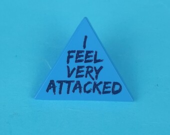 May include: A blue triangular die with the text "I FEEL VERY ATTACKED" written in black.