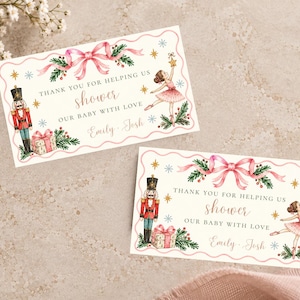 May include: Two rectangular thank you cards featuring a watercolor illustration of a nutcracker, a ballerina, a pink ribbon, pine branches, and gold stars. The text reads: THANK YOU FOR HELPING US shower OUR BABY WITH LOVE Emily - Josh.