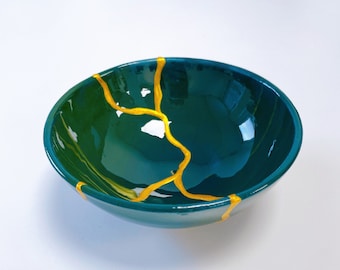 May include: A teal green ceramic bowl with a gold crackle design. The bowl is round and has a smooth, glossy finish.