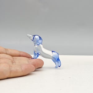 May include: A small, clear glass dog figurine with blue accents. The dog is standing, with its head raised. The figurine is approximately 2 inches long.
