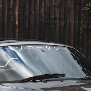 Può includere: Un'auto sportiva grigia con un parabrezza che ha un adesivo bianco con il testo giapponese "フロン".