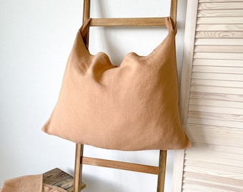 May include: A large, light brown linen pillow is hanging on a wooden ladder. The pillow is made of a soft, natural fabric and has a relaxed, casual look.