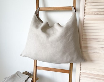 May include: A large, beige linen cushion with a simple, rectangular shape. The cushion is hanging on a wooden ladder.