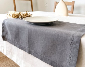 Puede incluir: Un camino de mesa de lino gris con un borde cosido se encuentra sobre un mantel blanco. Un plato blanco y un jarrón con tallos de trigo secos están sobre la mesa.