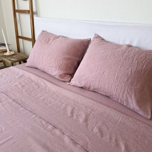 Op de afbeelding: Een stofvormig roze linnen beddengoedset met twee kussenslopen en een plat laken. Het beddengoed is gemaakt van een zachte, ademende stof en perfect voor een knusse nachtrust.