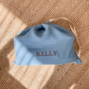 May include: A light blue linen drawstring bag with the name "Kelly" embroidered in dark gray thread.