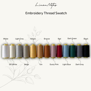 May include: A thread color chart with 12 spools of embroidery thread. The colors are white, light grey, yellow, bronze, red, dark green, black, off white, beige, tan, dusty pink, light blue, and dark grey.