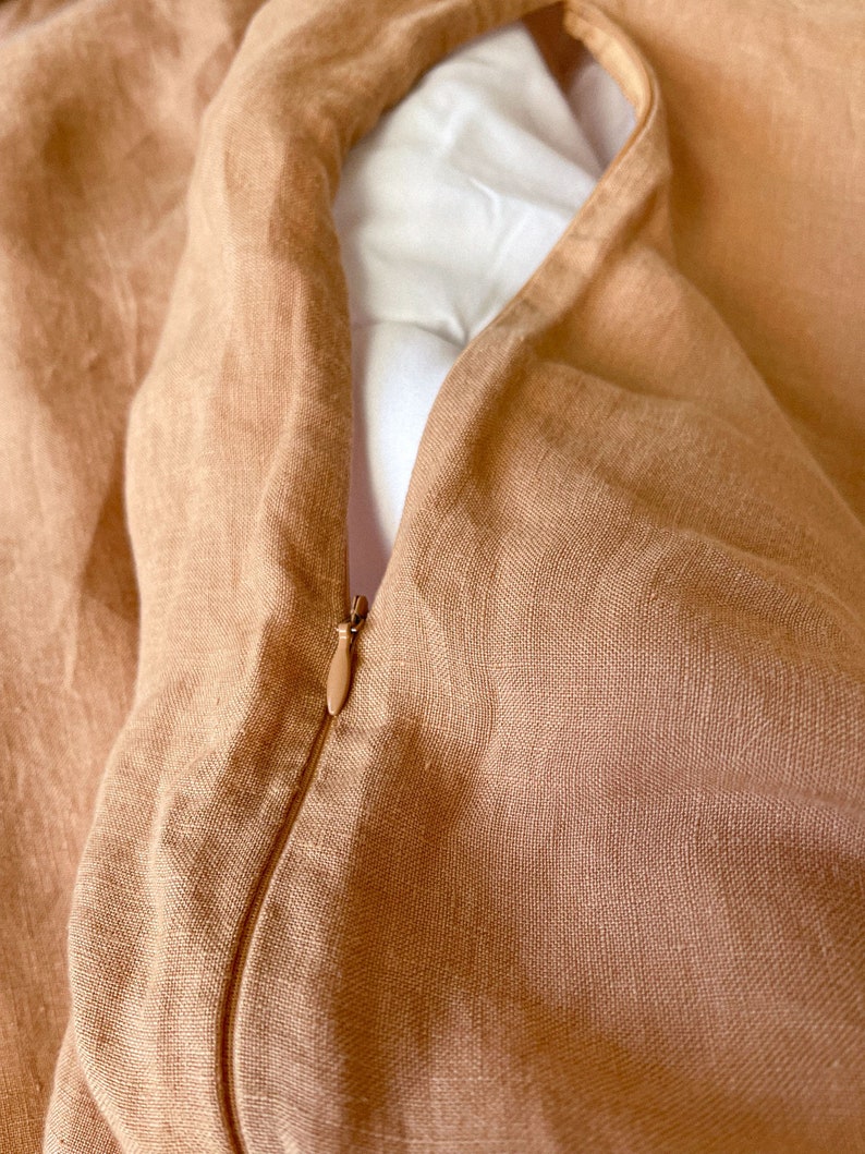 May include: A close-up of a tan linen duvet cover with a zipper closure. The zipper is visible and the fabric is textured.