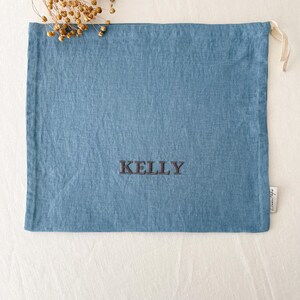 May include: A blue linen drawstring bag with the name "KELLY" embroidered in black thread.