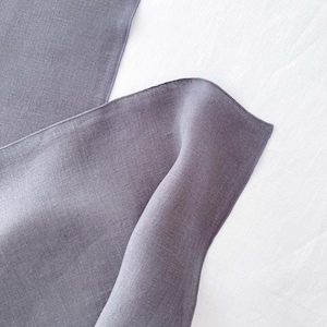 Peut inclure: Deux morceaux de tissu en lin gris foncé pliés et disposés sur une surface blanche.