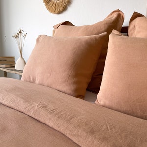 May include: A close-up of a bed with a terracotta-colored linen duvet cover and matching pillowcases. The bed is made with a simple, relaxed style.
