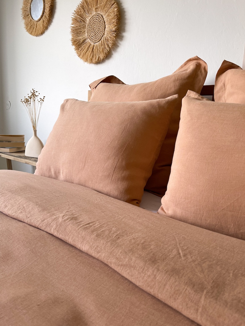 May include: A close-up of a bed with a terracotta-colored linen duvet cover and matching pillowcases. The bed is made with a simple, relaxed style.