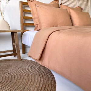 May include: A light brown linen duvet cover and pillowcases on a bed with a wooden headboard. A round jute rug is on the floor in front of the bed.