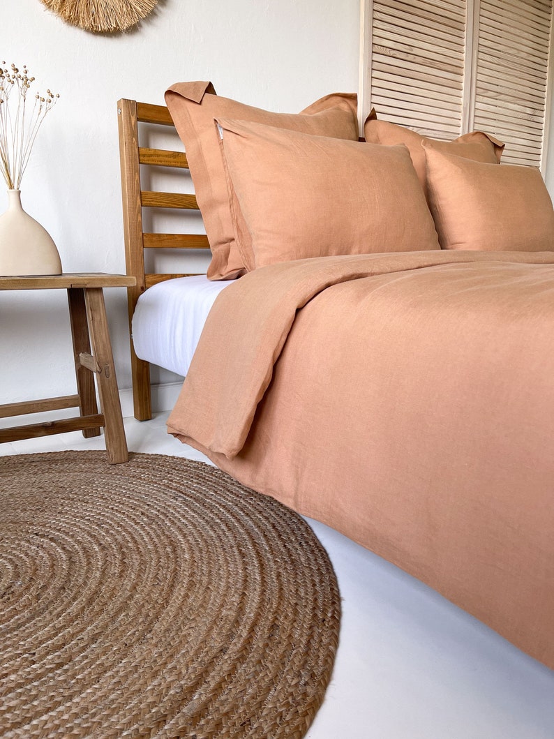 May include: A light brown linen duvet cover and pillowcases on a bed with a wooden headboard. A round jute rug is on the floor in front of the bed.