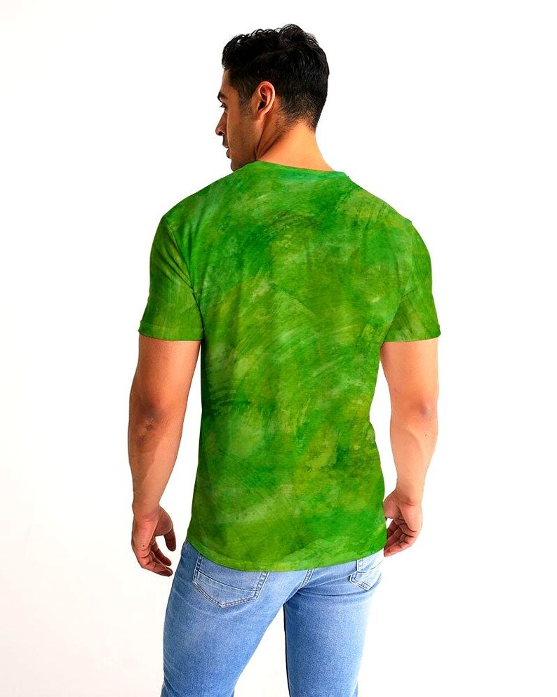 May include: A green t-shirt with a textured, watercolor-like design. The shirt is short-sleeved and has a crew neck. The model is wearing blue jeans.