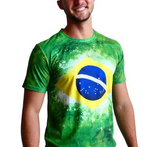 May include: Green t-shirt featuring the Brazilian flag. The shirt has a vibrant green background with white accents and the flag's yellow diamond, blue circle, and star pattern prominently displayed on the front.