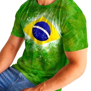 May include: Green t-shirt featuring the Brazilian flag. The shirt has a yellow diamond with a blue circle and white stars in the center. The shirt is a vibrant green with a watercolor effect.