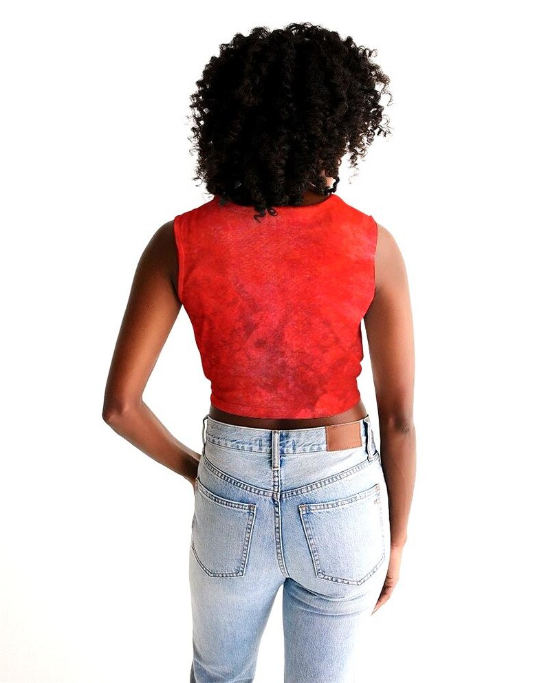 May include: A sleeveless red crop top with a textured pattern. The top is paired with light blue denim jeans. The model is facing away from the camera, with hands in the pockets of the jeans.