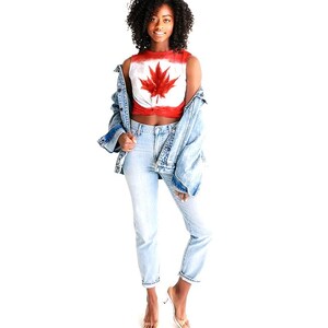 May include: A red and white crop top with a large red maple leaf design. The top is paired with light blue jeans and a denim jacket. The person is wearing clear heeled sandals.