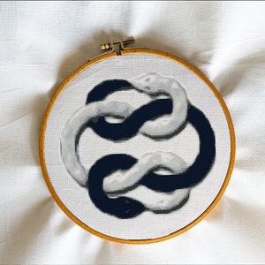 May include: A black and white embroidery hoop with a design of two intertwined snakes. The snakes are in a continuous loop, creating a symbol of infinity.