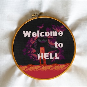 May include: A black embroidery hoop with a cross-stitch design that says "Welcome to HELL" in white text. The design features a dark figure standing in front of a fiery landscape.