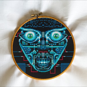 Könnte beinhalten: Kreuzstich-Stickerei eines Robotergesichts in einem Holzreifen. Das Design zeigt einen schwarzen Hintergrund mit einem detaillierten Gesicht in Blau- und Türkistönen mit roten Akzenten. Die Augen sind groß und detailliert.