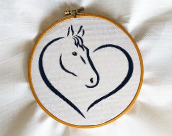 May include: A black and white embroidery of a horse's head inside a heart shape, displayed in a wooden embroidery hoop.