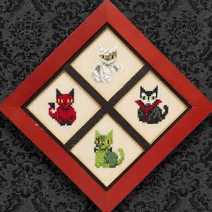 May include: A red frame with four black and white cross-stitch images of cats dressed in Halloween costumes. The cats are dressed as a mummy, a vampire, a devil, and a zombie. The text "PDF Pattern Instant Download" is at the bottom of the image.