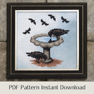 May include: A cross-stitch pattern of a bird bath with a bird perched on the edge and five birds flying overhead. The bird bath is brown and white with a blue water basin. The birds are black. The pattern is framed in a black frame.