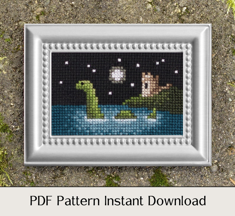 May include: A framed cross-stitch pattern depicting a green sea monster swimming in blue water beneath a starry night sky. The pattern also includes a small brown castle on a green island.