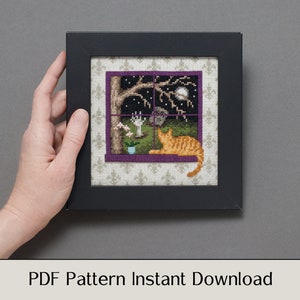 May include: A cross-stitch pattern featuring a window with a cat looking out at a night scene with a full moon, stars, and a tree. The pattern is framed in a black frame with a purple mat.