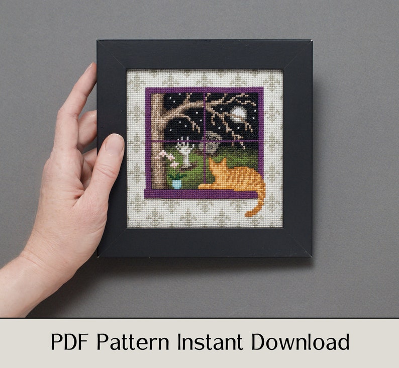 May include: A cross-stitch pattern featuring a window with a cat looking out at a night scene with a full moon, stars, and a tree. The pattern is framed in a black frame with a purple mat.