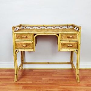 May include: A light brown bamboo desk featuring a woven cane surface and four drawers with small bamboo handles. The desk includes a decorative lattice railing along the back and sides, supported by four sturdy bamboo legs with cross-bracing.