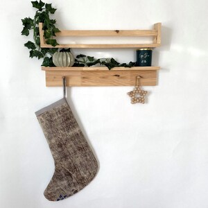 May include: A wooden shelf with two tiers, a decorative star, and a stocking hanging from a hook. The shelf is made of natural wood and has a rustic look. The stocking is made of a patterned fabric and has a grey cuff.