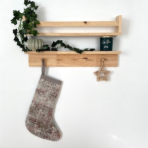 Op de afbeelding: Een houten plank met twee planken en een haak. Een groene kaars pot staat op de bovenste plank. Een kous hangt aan de haak. Een houten ster ornament hangt aan de onderste plank.