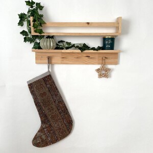 May include: A wooden shelf with two tiers, a decorative star, and a stocking hanging from a hook. The shelf is made of natural wood and has a rustic look. The stocking is brown and patterned with a white trim.