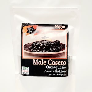 May include: A white pouch of Mole Casero Oaxaqueño, a Mexican black mole. The label features an image of the mole dish, the text "Negro", and the words "Oaxacan Black Mole". Net weight is 1 lb (454g).