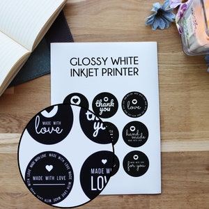 May include: A sheet of glossy white sticker paper with black and white round stickers printed with various phrases, including "Made with Love", "Thank You", "Love", "Handmade", and "For You".