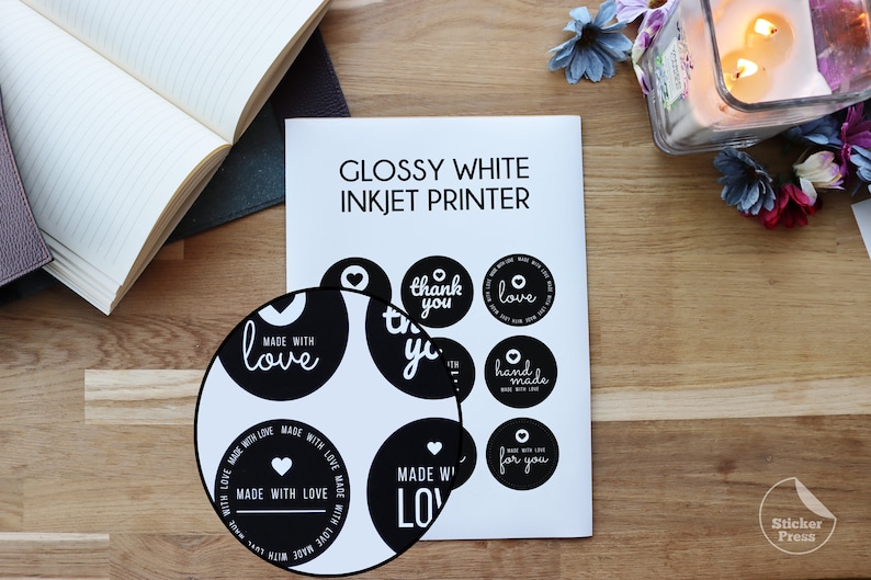 May include: A sheet of glossy white sticker paper with black and white round stickers printed with various phrases, including "Made with Love", "Thank You", "Love", "Handmade", and "For You".