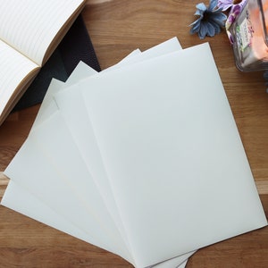 May include: A stack of four white blank sheets of paper on a wooden surface. The paper is smooth and has a slight sheen. The paper is perfect for writing, drawing, or crafting.