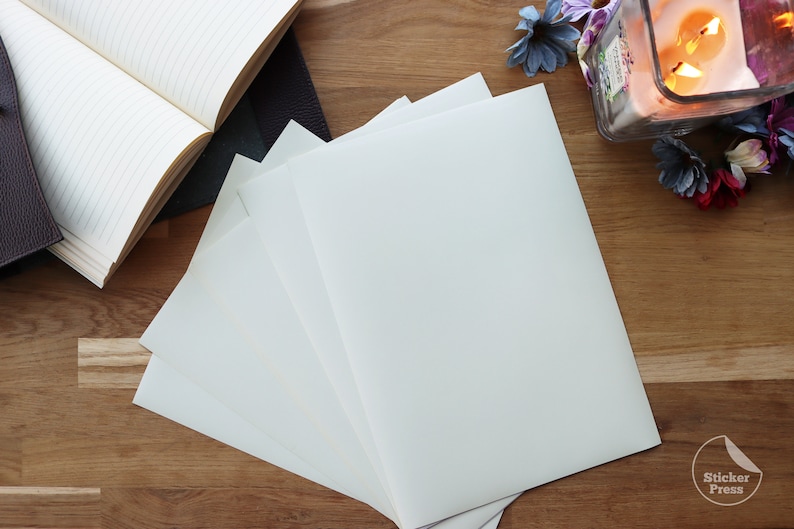 May include: A stack of four white blank sheets of paper on a wooden surface. The paper is smooth and has a slight sheen. The paper is perfect for writing, drawing, or crafting.