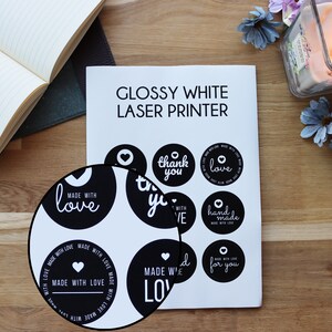 May include: A sheet of glossy white sticker paper with black and white circle stickers printed with various phrases, including "made with love", "thank you", "love", and "handmade".