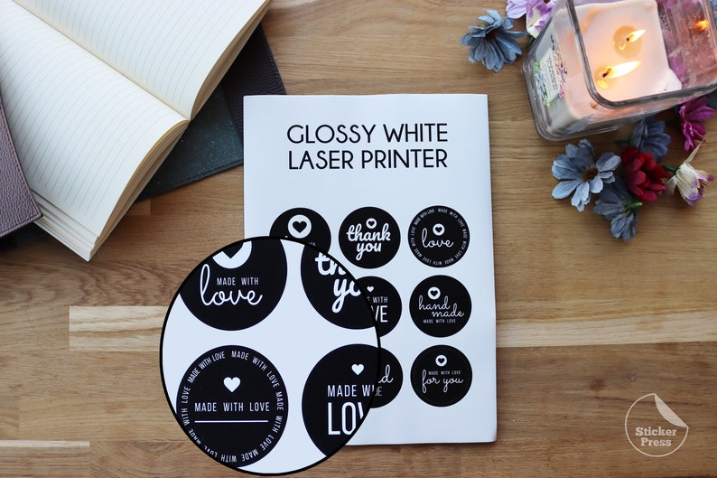 May include: A sheet of glossy white sticker paper with black and white circle stickers printed with various phrases, including "made with love", "thank you", "love", and "handmade".