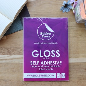 May include: A package of 25 sheets of white gloss self-adhesive inkjet and laser printable label sheets. The package is purple with the text "Sticker Press" and "quality stickers and labels". The package also says "GLOSS white SELF ADHESIVE inkjet and laser printable label sheets WWW.STICKERPRESS.CO.UK 25 A4"