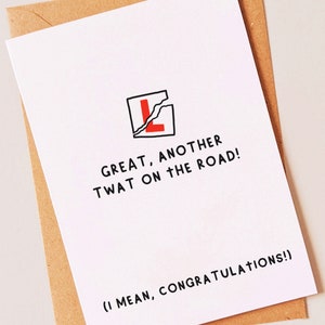 May include: A white card with a black and red illustration of a cracked L-plate. The text on the card reads "GREAT, ANOTHER TWAT ON THE ROAD! (I MEAN, CONGRATULATIONS!)"