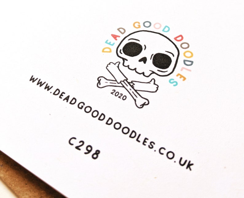 May include: A white card with a black and white illustration of a skull and crossbones. The skull is smiling and giving a thumbs up. The text "Dead Good Doodles" is written in a circle around the skull, with each letter in a different color. The text "www.deadgooddoodles.co.uk" is written below the skull and crossbones. The text "C298" is written below the website address.