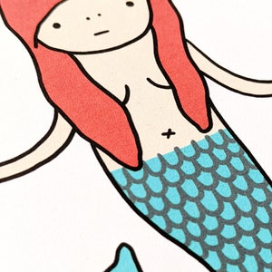 May include: A cartoon illustration of a mermaid with red hair and a blue and gray fishtail.